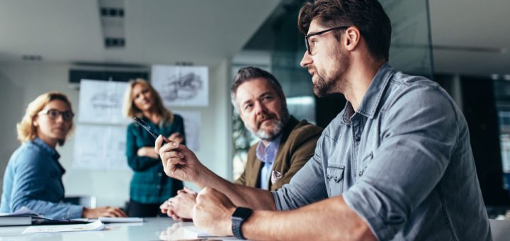 Young designer giving some new ideas about project to his partners in conference room. Business people discussing over new business project in office.