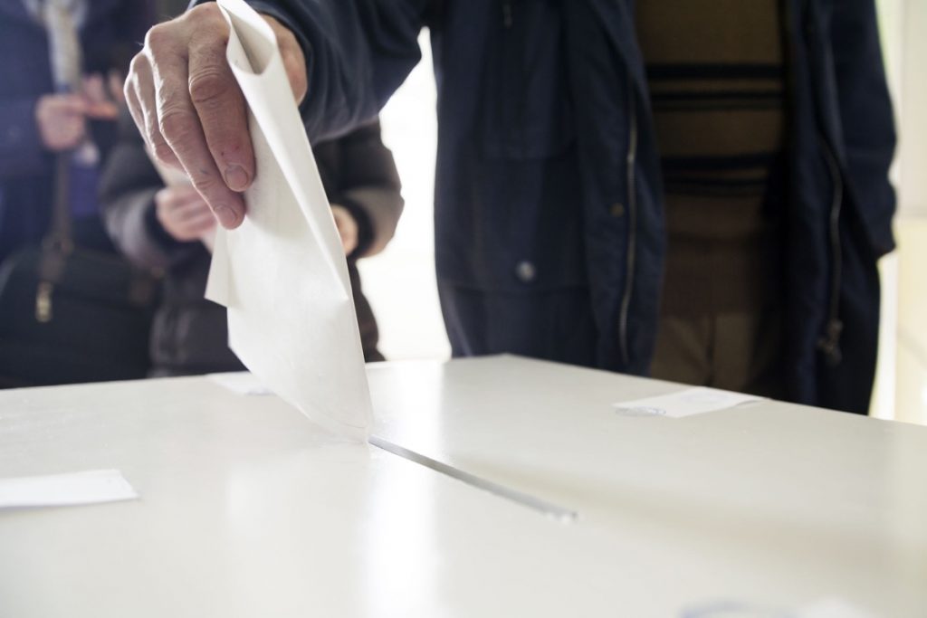 Hand of a person casting a ballot at a polling station during voting.