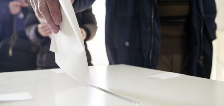 Hand of a person casting a ballot at a polling station during voting.