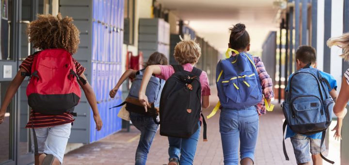 School kids running in elementary school hallway, back view