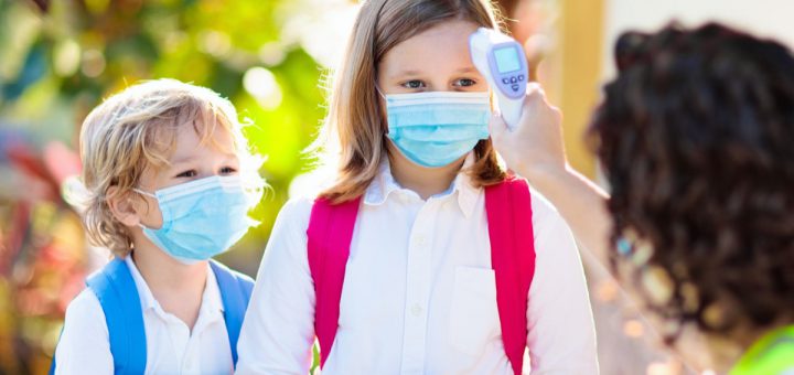 Temperature screening and medical check at school. Child in face mask in class in covid-19 outbreak. Teacher with thermometer at preschool entrance. Social distancing. Coronavirus prevention.