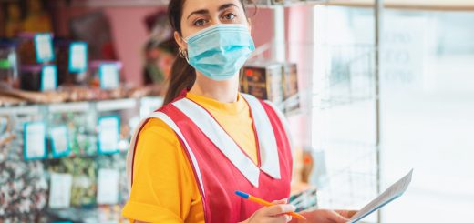 Food store. Portrait of a female employee in uniform with a medical mask on her face, holding documents. The concept of protecting against coronavirus at work.