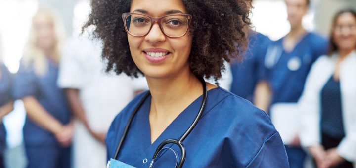 Young black female doctor looking at camera in a hospital standing in front of medical team