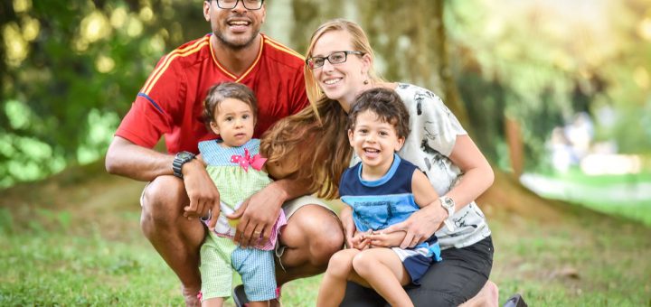 Happy interracial family is enjoying a day in the park. Little mulatto baby girl and boy. Successful adoption. Diverse family in nature with sun in the back.
