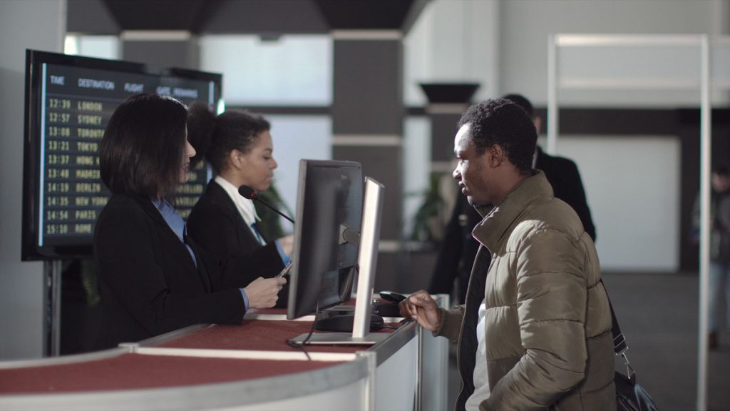 Two female airport security personnel checking identification at a check-in or boarding counter at the departure terminal holding the passports of two male passengers