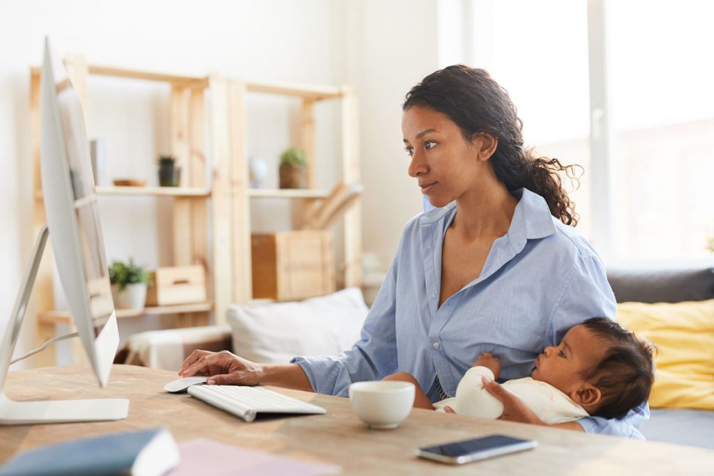 mother sitting at desk and working on project while nursing baby