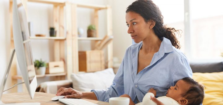 mother sitting at desk and working on project while nursing baby