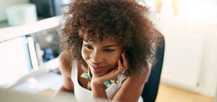Black smiling girl using small business computer on blurred inside background.