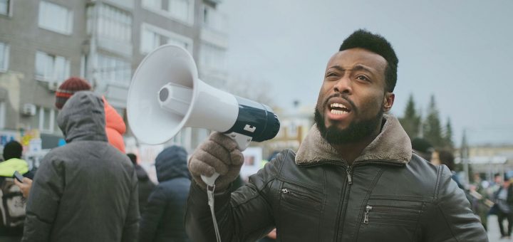 African american man hold megaphone hand and shouting. Crowd people day demonstration. Afro rebel strike protest. Revolution city street. Political rally. Loudspeaker shout. Activists outdoor fight.