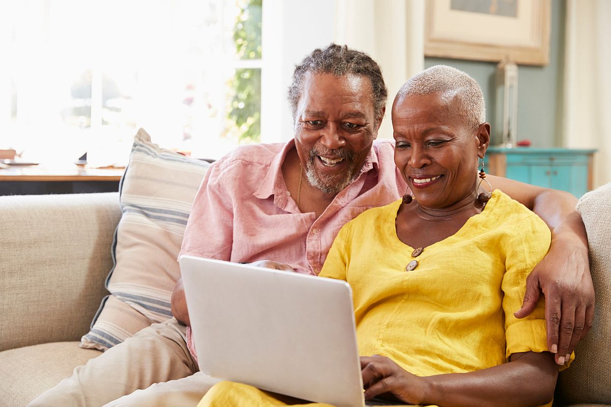 Senior Couple Sitting On Sofa Using Laptop At Home Together; Unions and Retirement Benefits concept