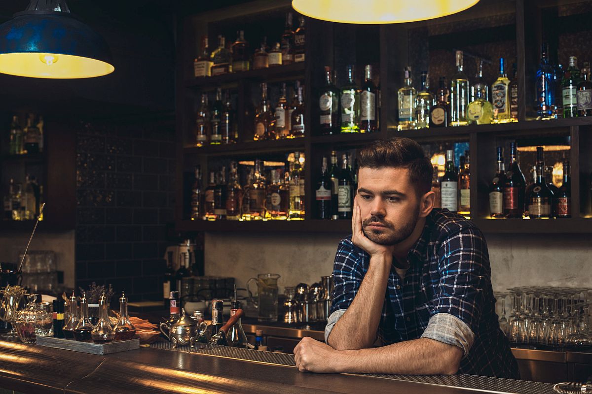 Young barman standing leaning on bar counter looking down thoughtful;
Great Resignation labor unions concept