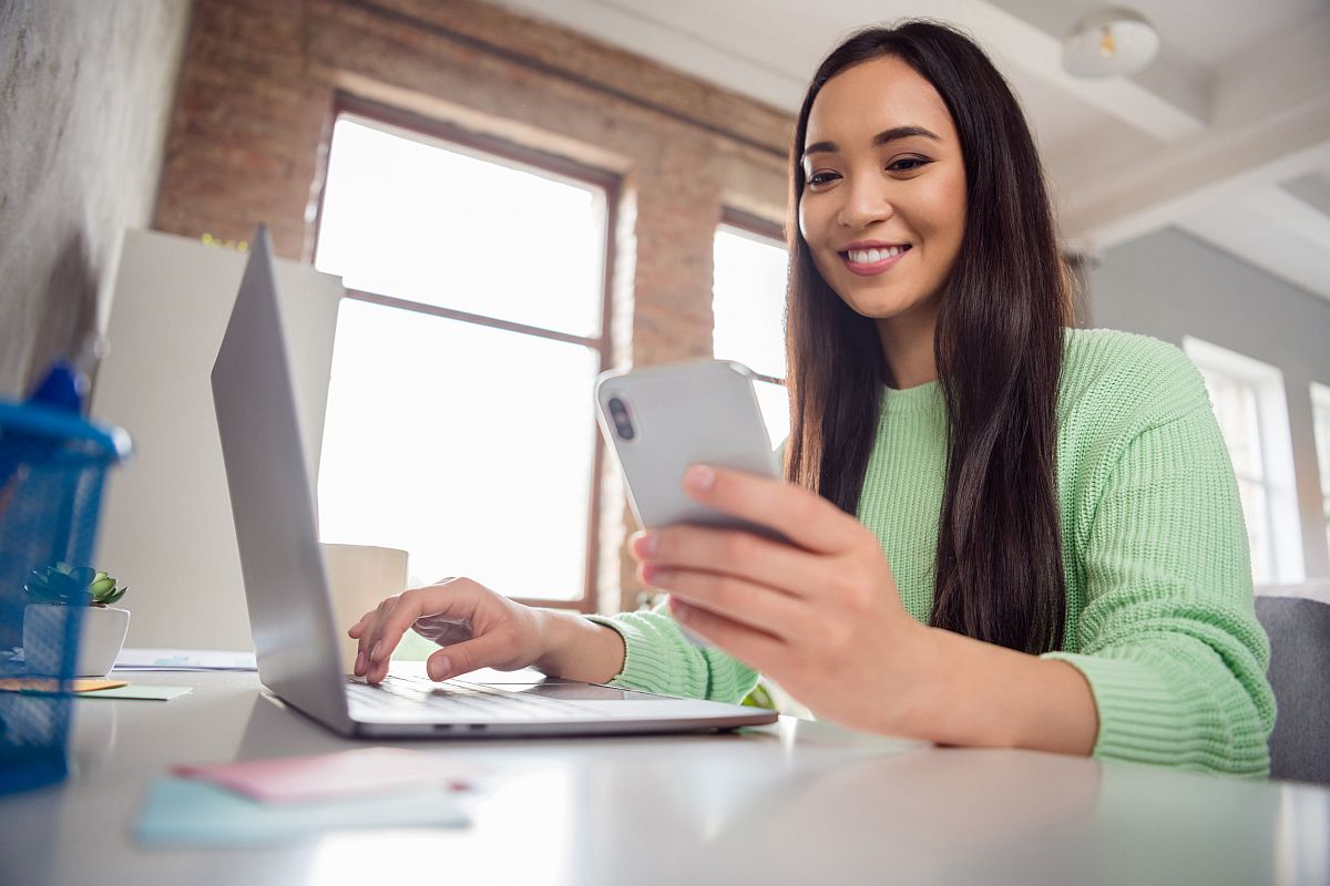 Low angle view of remote worker on laptop and checking smartphone; unions connect with digital natives concept