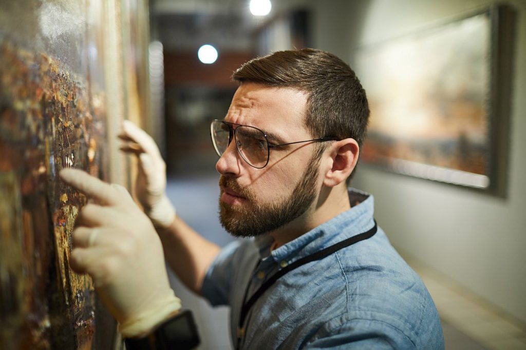 Man wearing gloves adjusting painting on wall; organizing in the culture sector concept