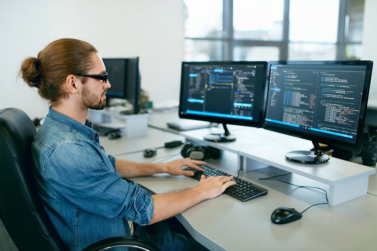 Person sitting at desk working on computer with two monitors; white-collar workers concept