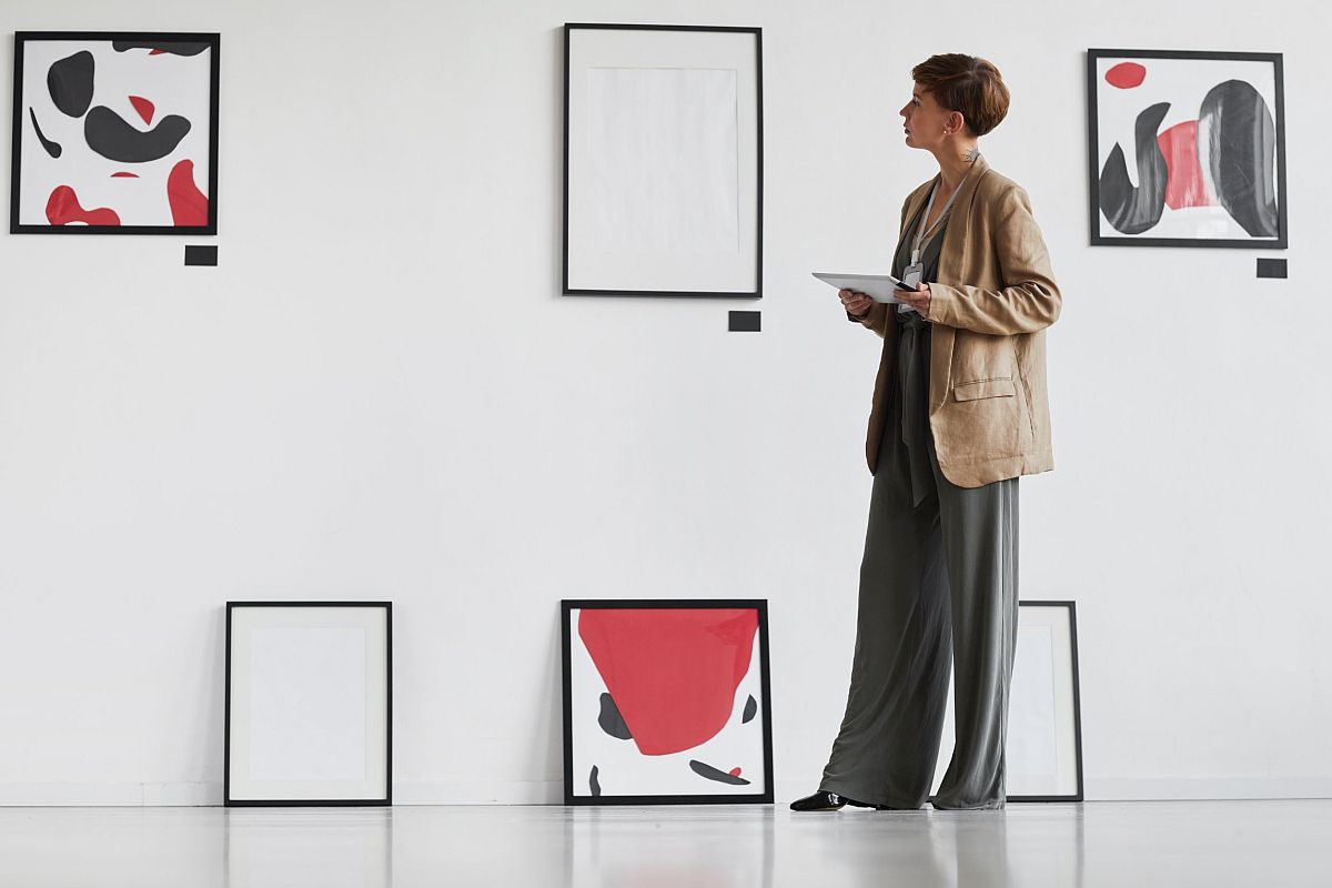 Woman in art gallery examining framed pictures on wall; organizing in the culture sector concept