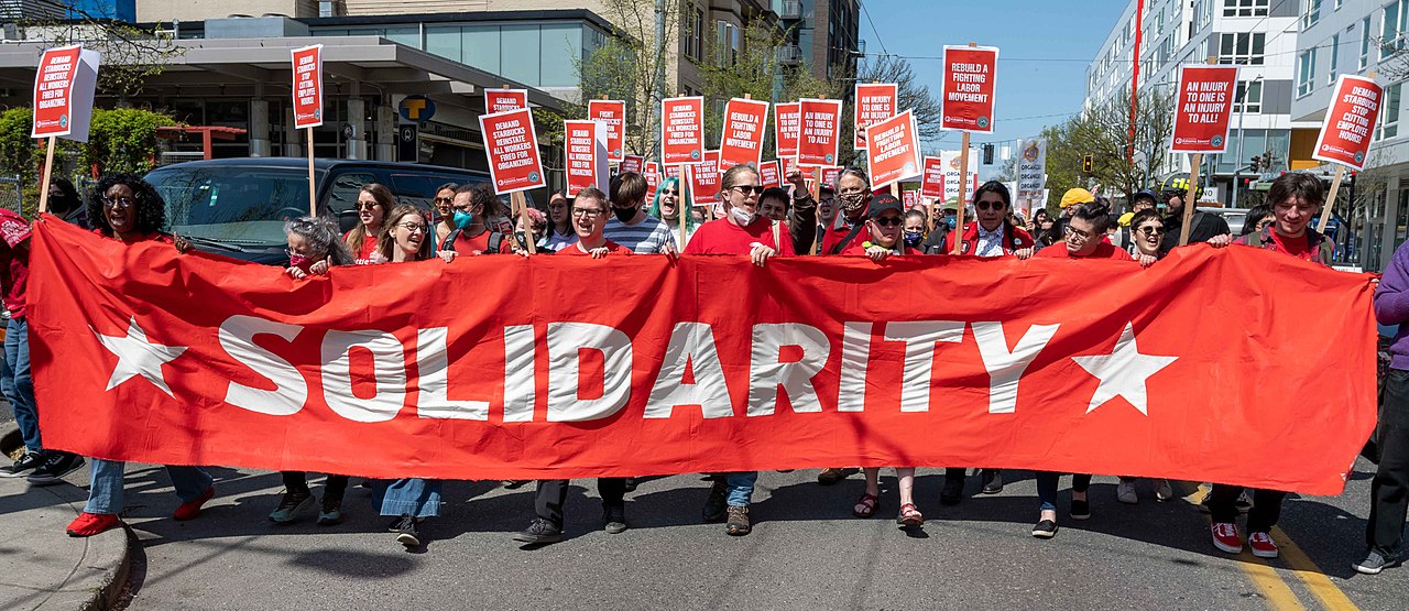 Large group of people marching with red Solidarity banner; young union organizers concept