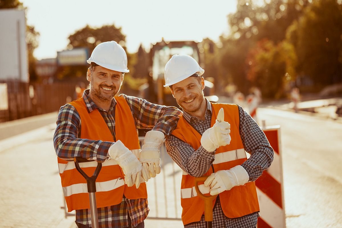 Two smiling workmen in orange vests and hard hats; new labor movement concept