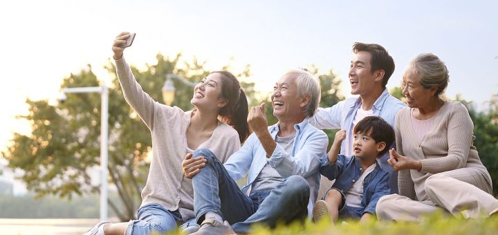 Three generations of a happy family sitting outdoors, taking a selfie; family benefits concept