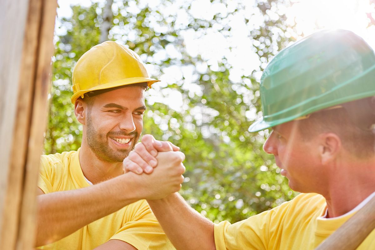 Two workmen in hard hats clasp hands; successful union election concept