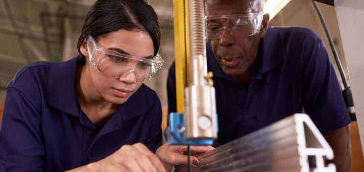 Young worker using tool, supervised by older worker; pro-worker initiatives concept