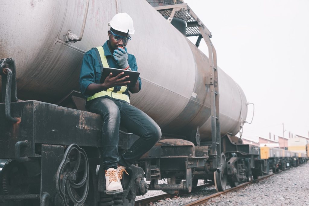 Engineer seated outside a train on a railway using walkie talkie and a tablet; rail unions concept