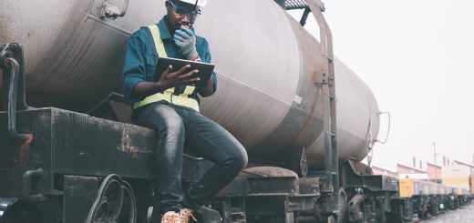 Engineer seated outside a train on a railway using walkie talkie and a tablet; rail unions concept