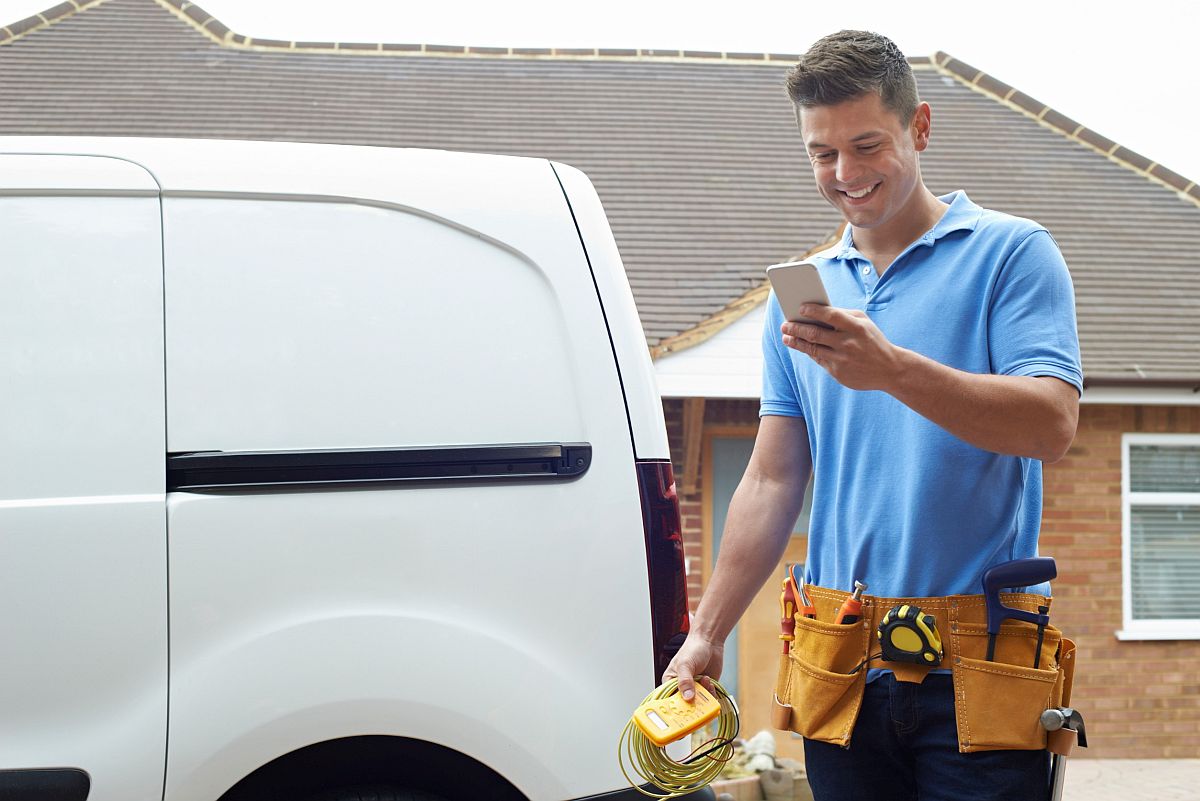 Smiling electrician leaving going to van and looking at his phone; social media concept