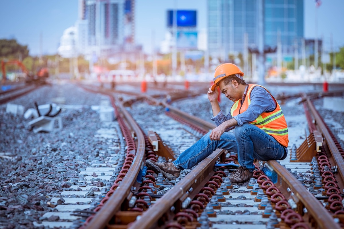 Unhappy-looking worker sitting on railroad tracks; preventable accident concept