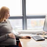 Pregnant woman sitting at her desk in the office; DOL initiatives concept