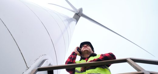 View from below of engineer wearing hard hat and reflective vest talking on mobile phone on wind turbine stairway; inflation reduction act benefits unions concept