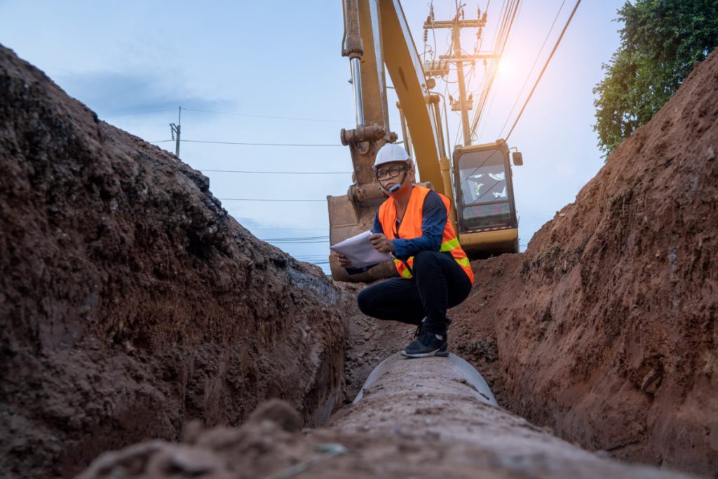 Engineer wear safety uniform examining excavation water supply or sewer pipeline at construction site; Department of Labor initiatives concept