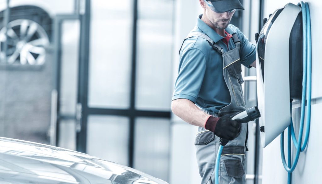 Worker plugging in electric vehicle; EV transition concept