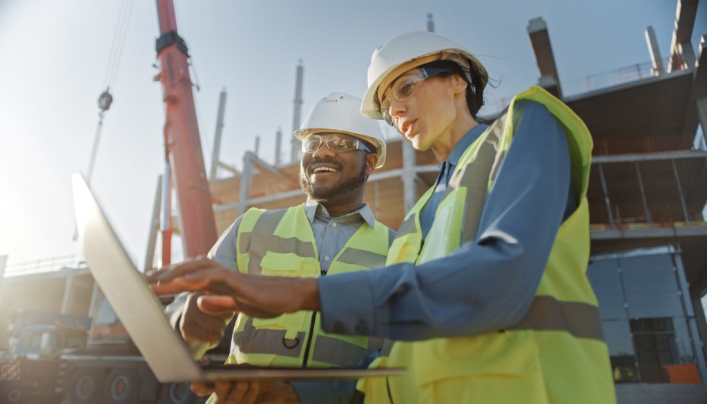 Engineer and supervisor at construction site checking tablet; workplace protection concept